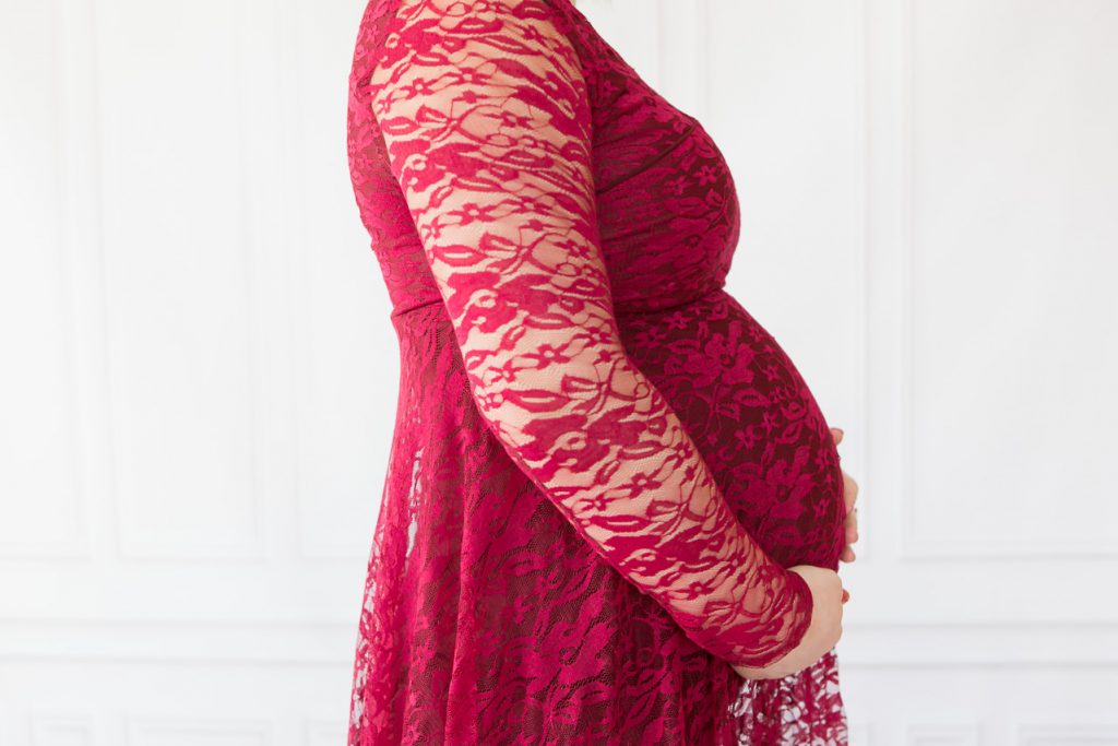 Detailaufnahme Babybauch von schwangeren Frau im roten Spitzenkleid