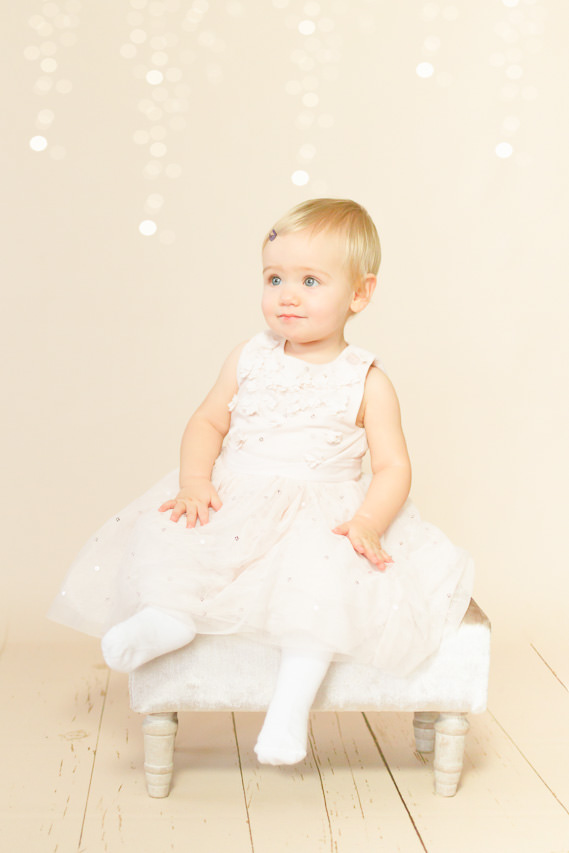 kleines mädchen sitzt auf einem hocker, sie trägt ein weißes kleid, kinderfotos ella photography erkrath