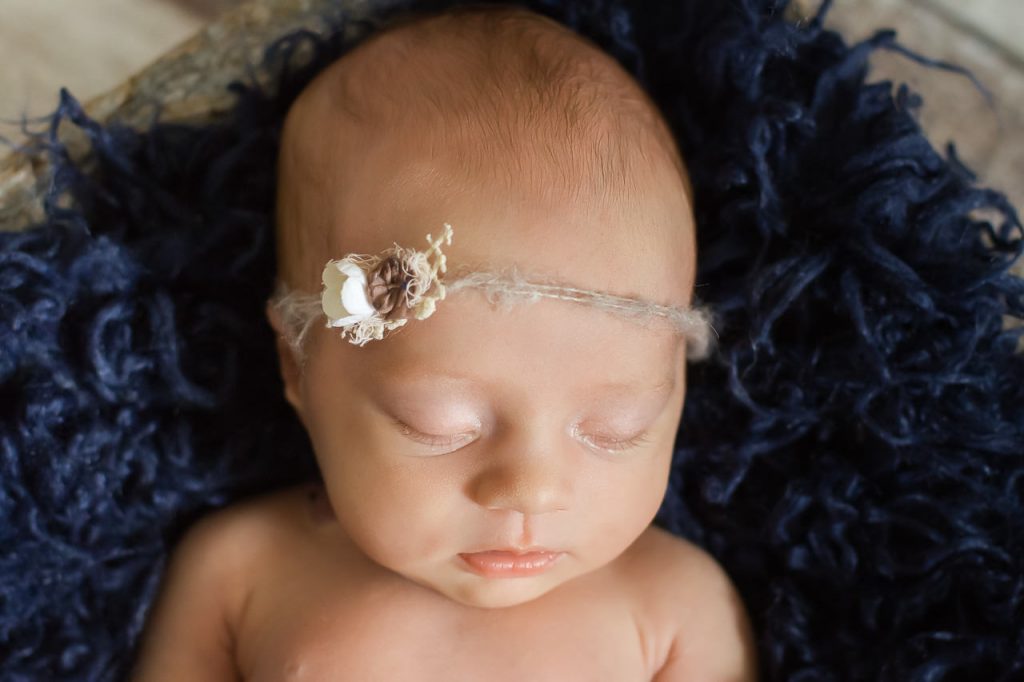 Neugeborenes liegt in einer Schale mit blauem fell und haarband und schläft. neugeborenenfotos von Ella Photography bei duesseldorf