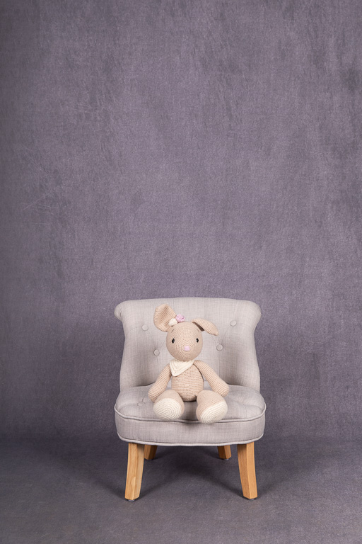 Ein kleiner Hase sitzt auf einem kleinen grauen Sessel vor einem grauen Hintergrund, ella photography erkrath
