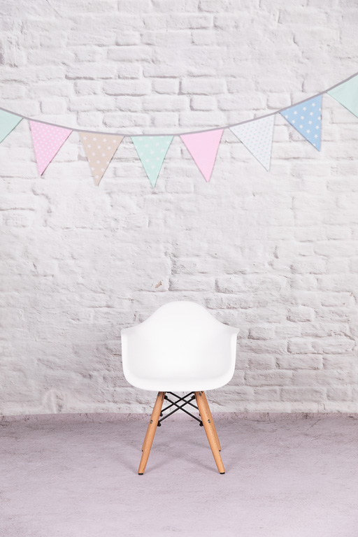 ein weißer Stuhl steht vor einer weißen Mauer, an der Mauer hängt eine pastellfarbene Wimpelkette, ella photography erkrath erkrath düsseldorf essen hilden